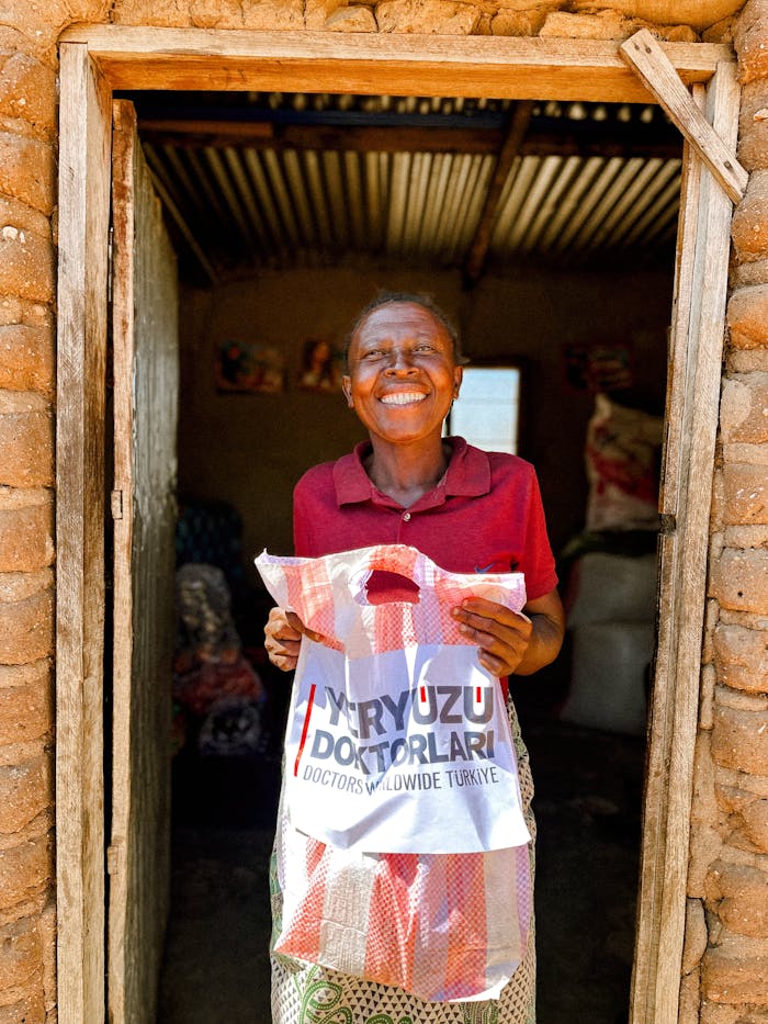 why-choose-us Smiling woman holds donation bag from Doctors Worldwide Turkey in a rustic setting.