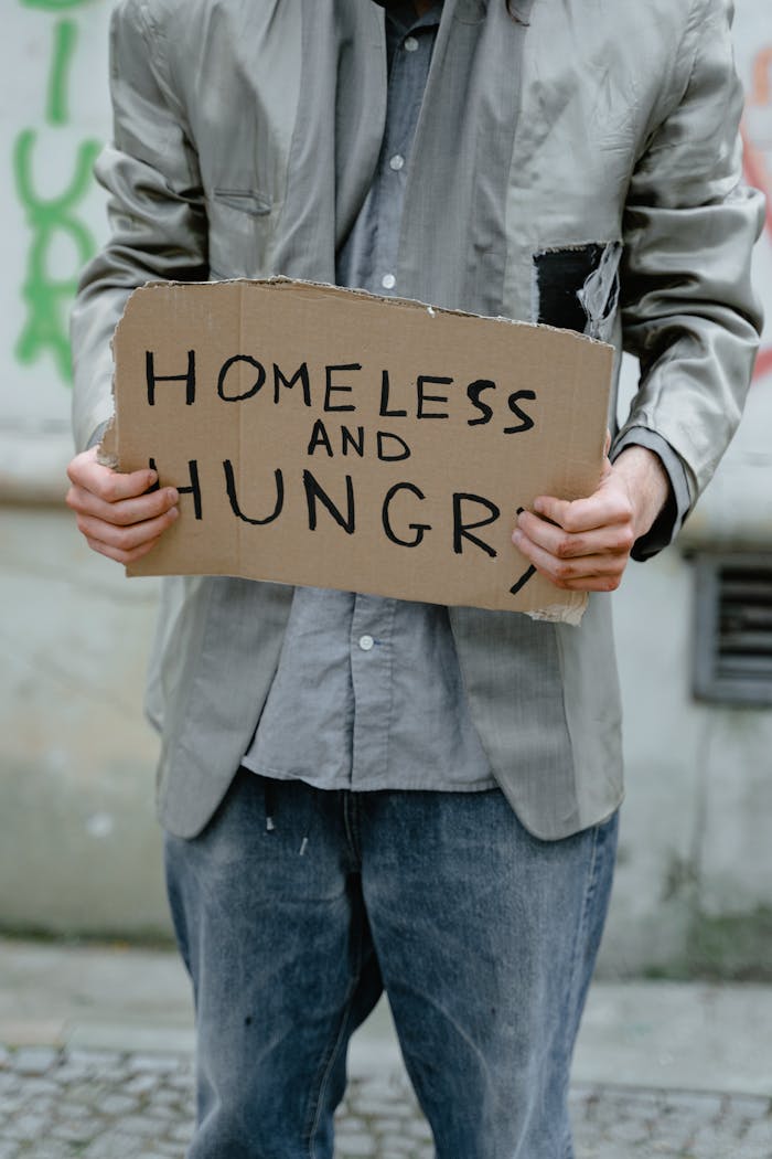 services-02 Person holding a 'Homeless and Hungry' sign, depicting urban poverty.