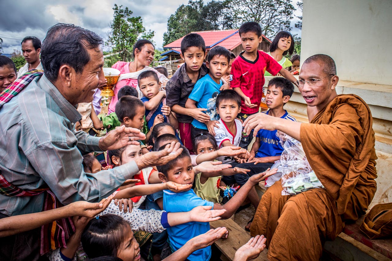 gallery-3 A monk interacts with a diverse group of people, sharing blessings outdoors.