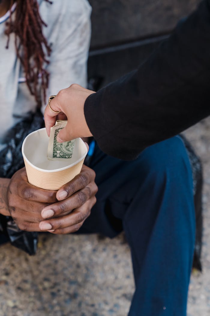 gallery-6 A person giving money to a homeless man seated outdoors in a gesture of compassion.